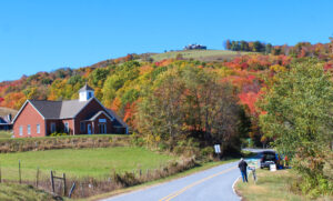 a beautiful brick home in the NC mountains, a hill behind the house is covered in trees that are changing in the fall